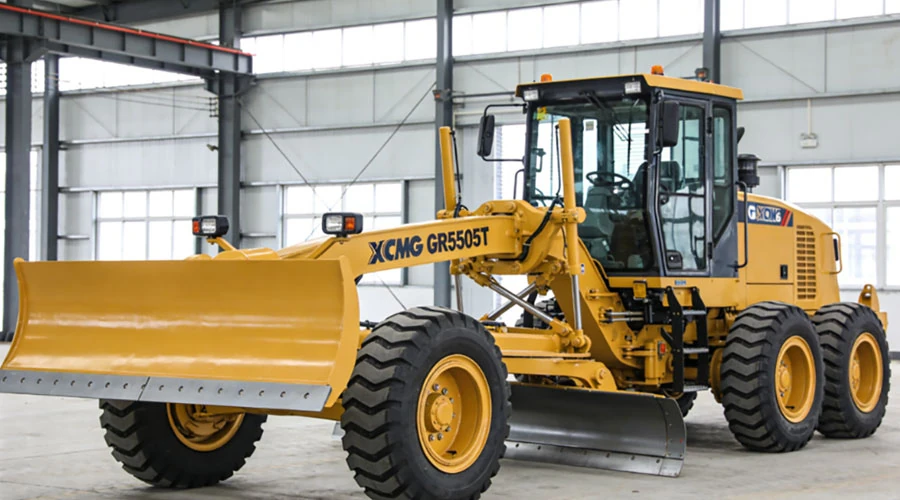 XCMG GR5505T motor grader displayed indoors, showing the front blade and rear wheels in a clean warehouse setting