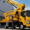 A yellow truck-mounted aerial boom lift with its platform extended to a building facade for maintenance work.