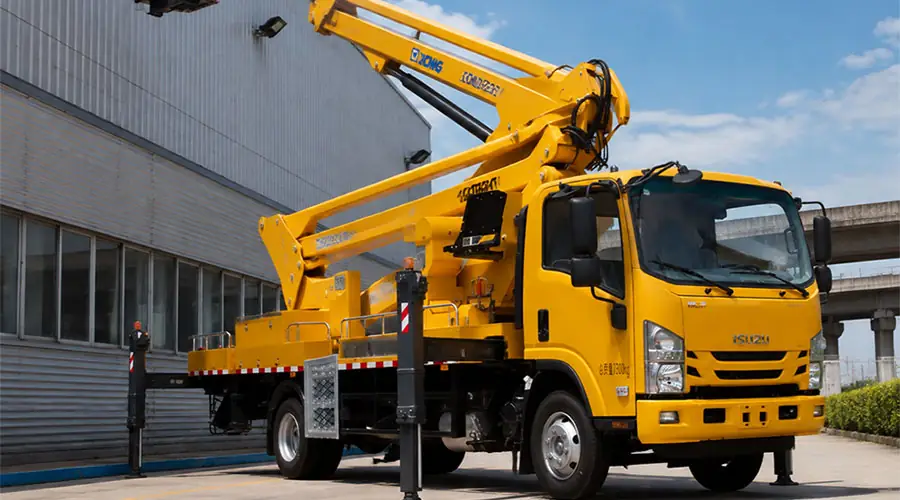 A yellow truck-mounted aerial boom lift with its platform extended to a building facade for maintenance work.