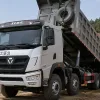 A white XCMG 8x4 heavy-duty dump truck tipping its cargo body to discharge materials at a construction and mining site.