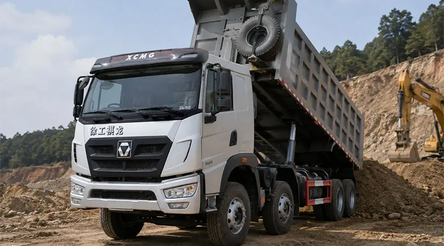 A white XCMG 8x4 heavy-duty dump truck tipping its cargo body to discharge materials at a construction and mining site.